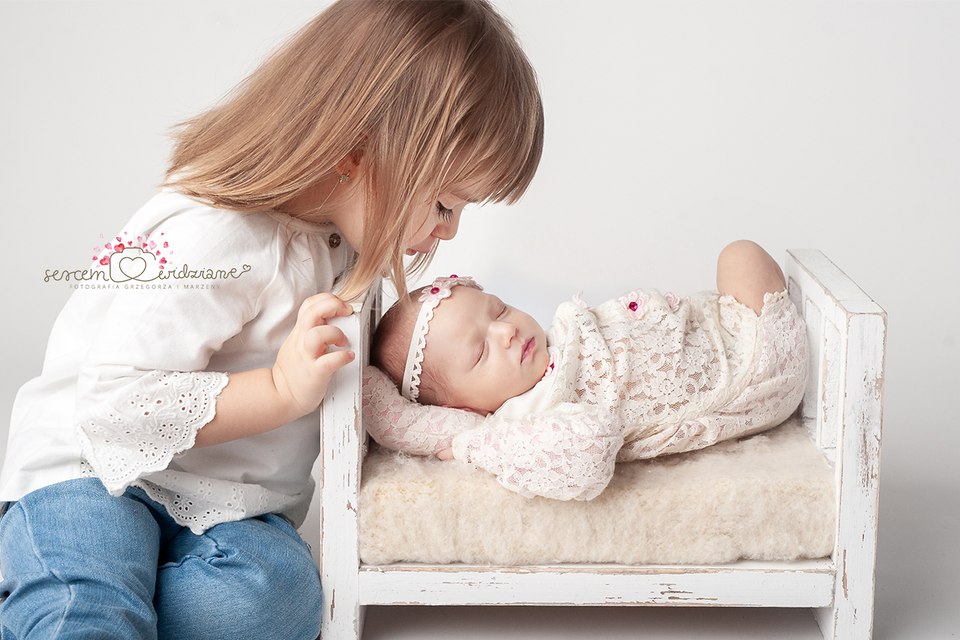 Liliana leży na łóżeczku na sesji noworodkowej a obok jest siostra
